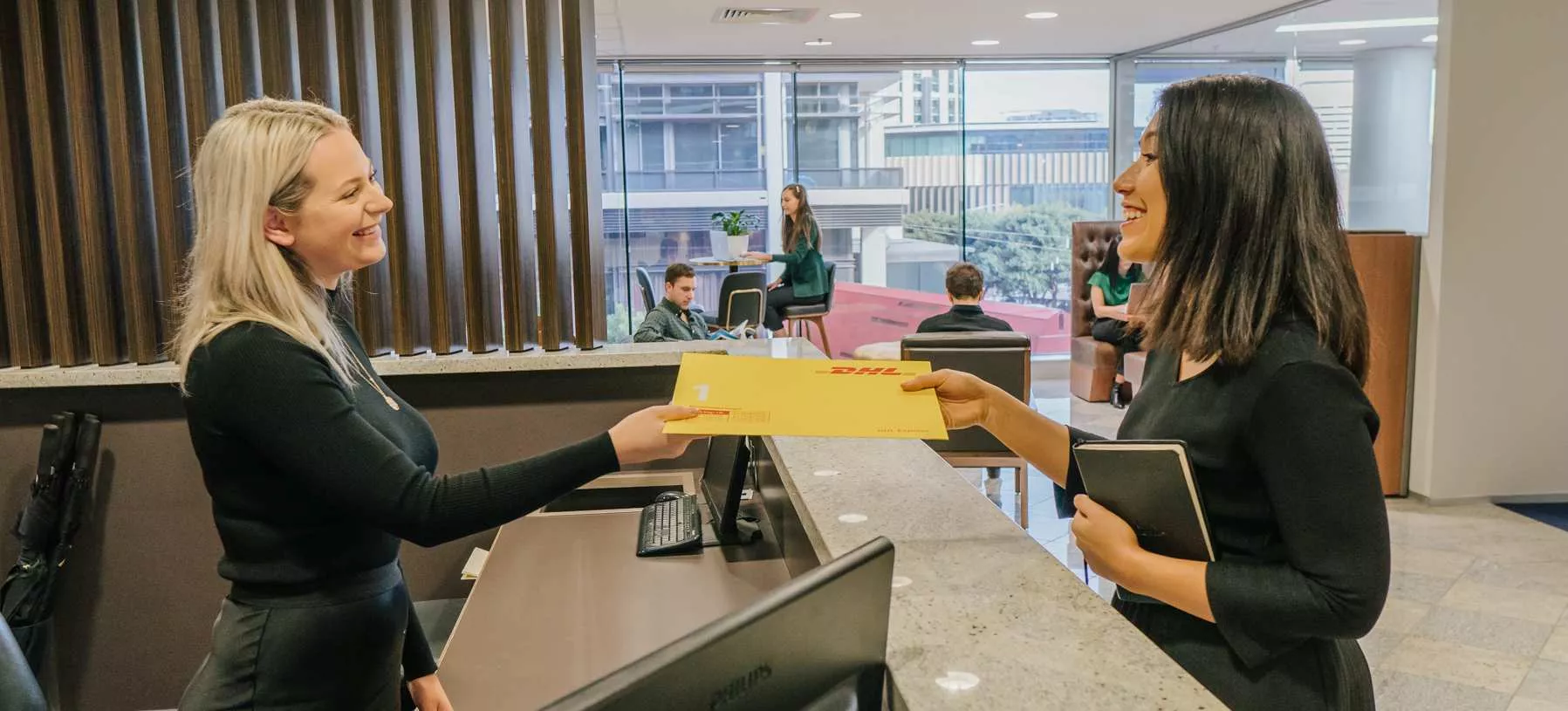 Receptionist hands over a mail envelope to a coworking client in a sleek office setting at Servcorp.